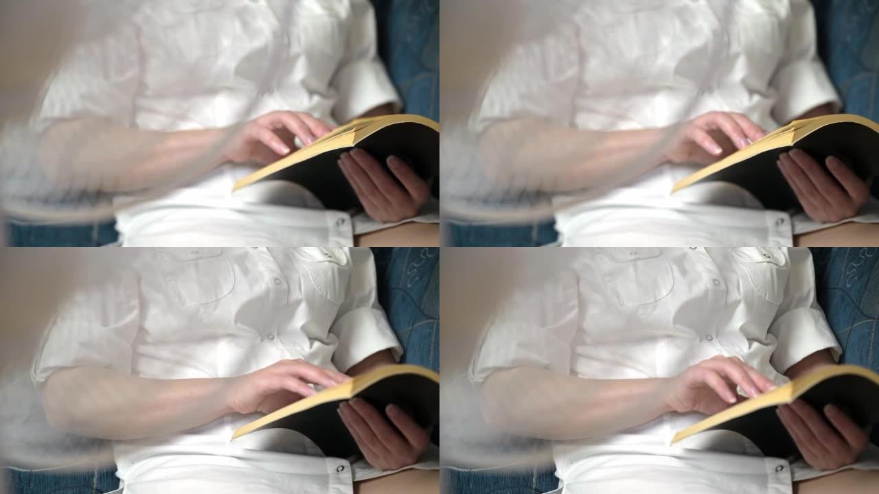 一个女人坐在扇子前读一本有趣的书。一只手和一本书的特写。