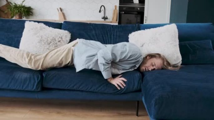 精疲力竭的年轻人在现代客厅舒适的沙发上睡着了，辛苦工作一天后没有精力。疲惫沮丧无动力的高加索人在家沙