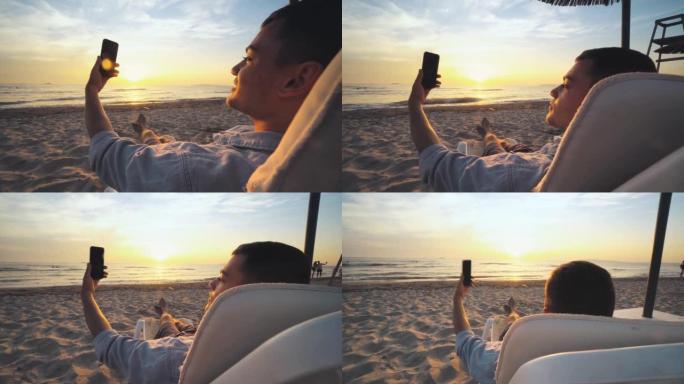 年轻人在日落，日出时在三一热带海滩上的躺椅上享受，并使用智能手机，度假和夏季旅行进行自拍照
