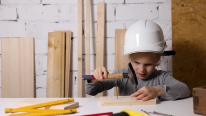 戴头盔的小女孩在木工车间学习在木板上钉钉子