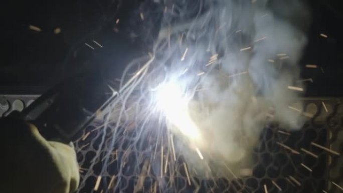 金属焊工的特写手与电弧焊机一起工作，在工厂用安全装置焊接钢材。火花和闪光飞舞。