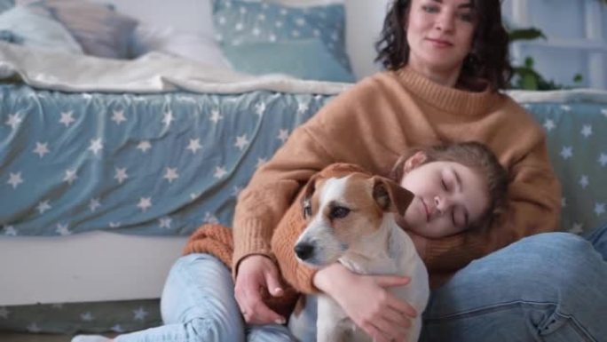 年轻的母亲和女儿穿着毛衣和狗杰克·罗素坐在地毯上的地板上，可爱的交流