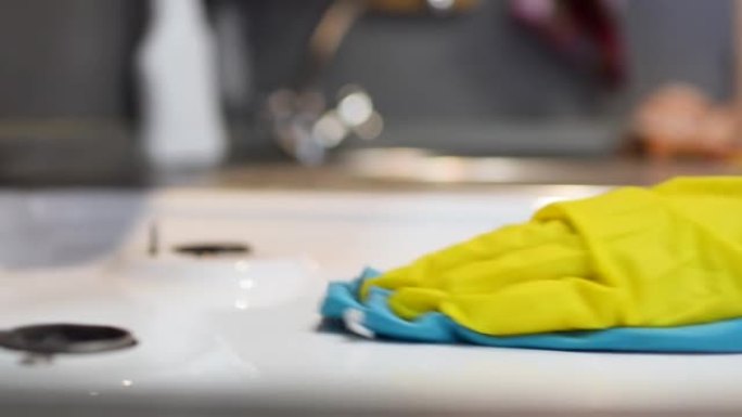 女人的手放在手套上用海绵清洗煤气炉，特写。清洁厨房内部