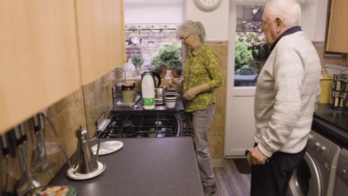 咖啡，谈话和退休，夫妻在厨房里聊天，并在早餐时间在家一起提供帮助。早上聊天，喝酒和老人残疾，女人泡茶