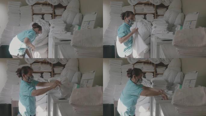 女工在酒店洗衣店装载洗衣机。在工业洗衣店工作的女人。员工用工业洗衣机装载衣物。