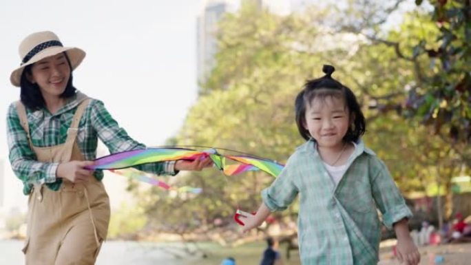 亚洲小儿子在沙滩上玩五颜六色的风筝，而美丽的亚洲妈妈则拿着风筝，跟着儿子奔跑，支撑着随风飘动的风筝。