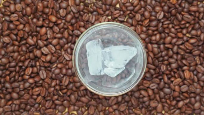 4k视频，将冰镇倒入带有咖啡豆背景的玻璃中的俯视图。冰冷咖啡的制备。