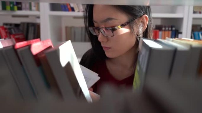 中国女学生在图书馆寻找书籍寻找大学工作研究的材料