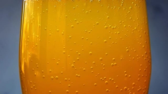 玻璃特写中的橙色苏打水气泡，灰色背景上有湿。湿玻璃配流行橙色苏打水。4k宏原始视频60 fps。
