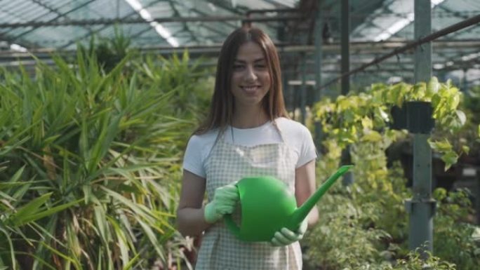 快乐的女性花店在围裙浇灌室内植物和鲜花。这个女孩在温室里照顾室内植物。照顾鲜花