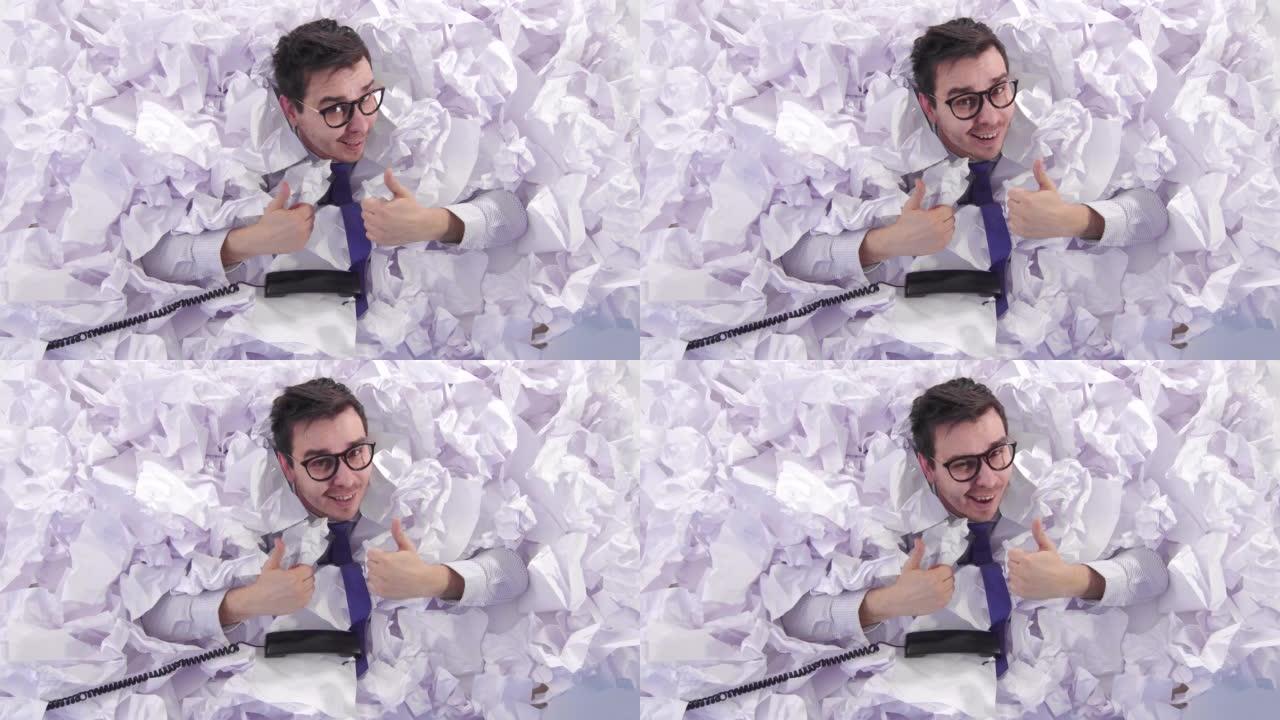 一名戴眼镜的男性白领正对着镜头竖起大拇指，在一大堆皱皱的纸上从上往下看
