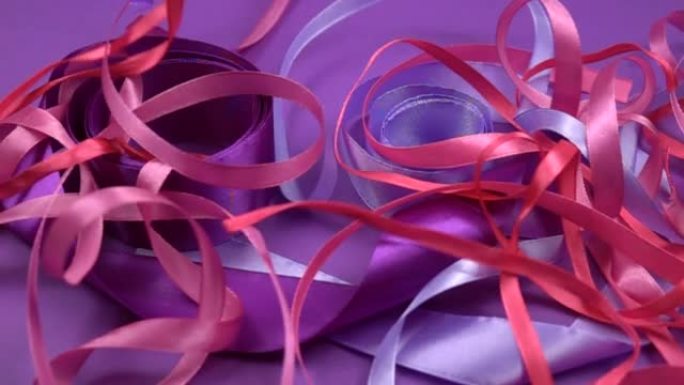 缎面紫色和粉色丝带躺在紫色背景上，慢动作