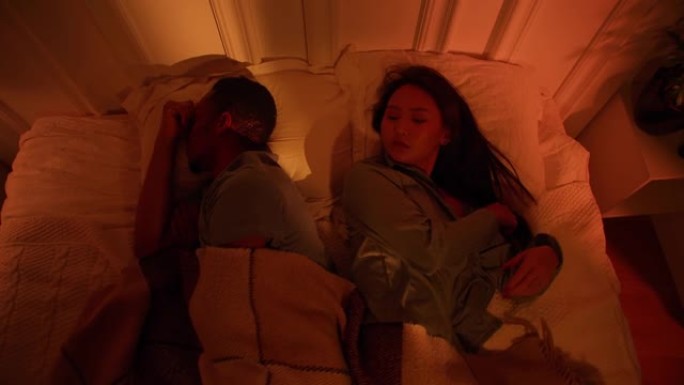 亚洲妇女和黑人男子正试图在嘈杂的公寓里打呼噜入睡
