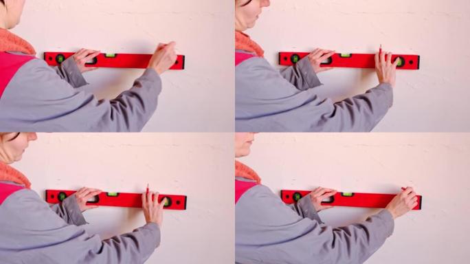 通过水平DIY家庭维修在墙上绘制水平标记。一名戴着红色棒球帽和建筑制服的妇女正在准备墙壁的装饰。