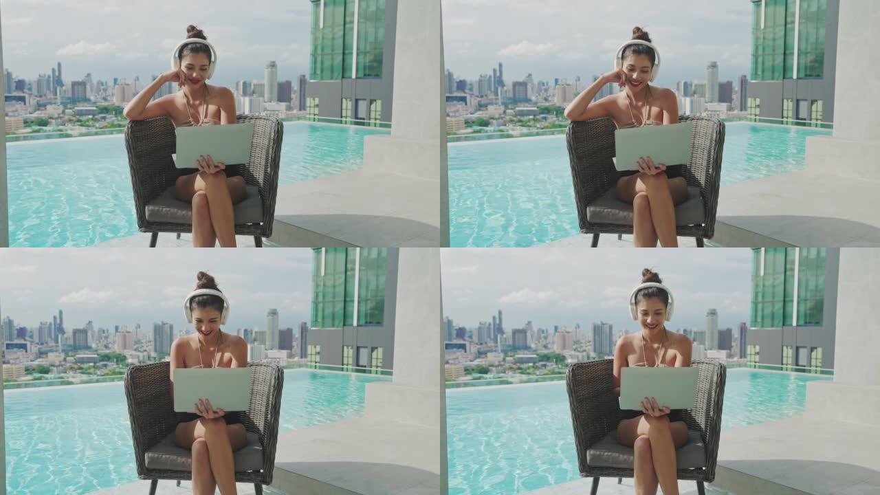 年轻的亚洲女性在夏天使用笔记本电脑坐在游泳池附近