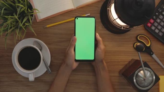 俯视图女人在智能手机的绿色屏幕上使用拇指触摸。爱好表背景。色度键。绿屏手机。