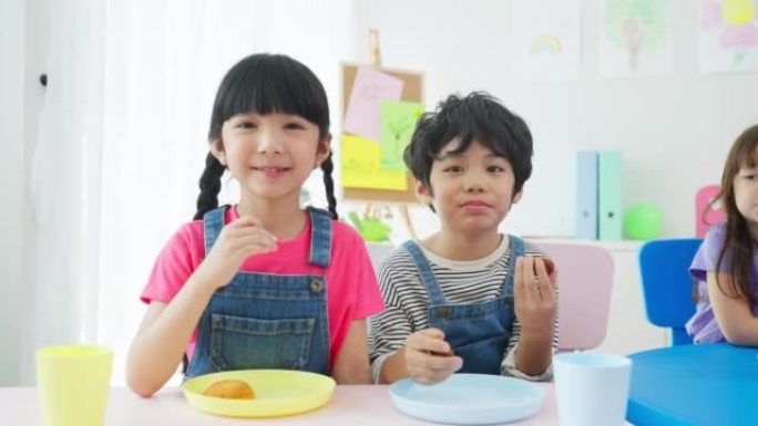 亚洲幼儿学生在餐桌上共进午餐的肖像。幼儿园的小学龄前男孩和女孩在课间休息时感到快乐并喜欢吃食物的混合