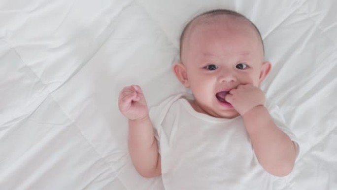 可爱的亚洲新生婴儿躺在白色床上玩耍的肖像看着相机，笑容满面。天真的小新婴儿可爱。