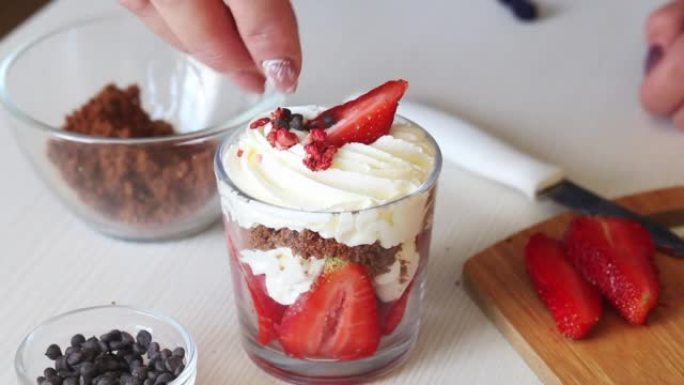 草莓配鲜奶油和脆饼。一名妇女用饼干屑和冻干草莓装饰甜点。添加巧克力滴。特写。