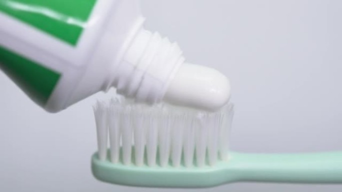 浴室里的特写镜头。将白色牙膏从管子中挤压到白色背景上的绿色牙刷上。刷牙。早晚程序。卫生。