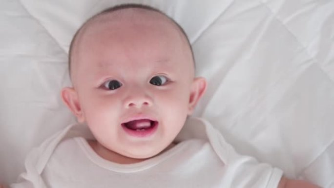 脸部特写肖像可爱的亚洲新生婴儿躺在白色床上玩耍看着相机笑着笑脸。天真的小新婴儿可爱。
