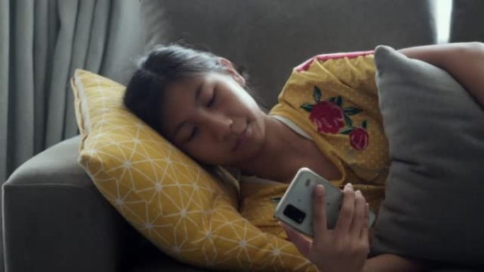 亚洲女孩在沙发上放松，在家使用靠近窗户的智能手机，生活方式理念。