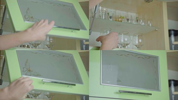男人用手打开厨房橱柜门，把玻璃放在架子上。关闭带玻璃门的现代厨柜，用于存放干净的餐具