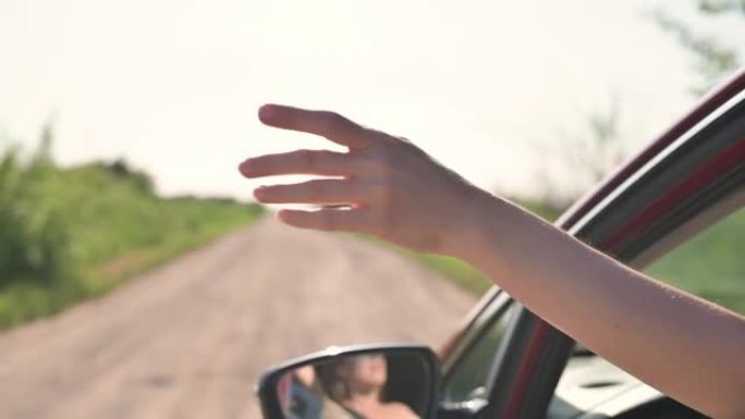 女孩从敞开的车窗上伸出手，捕捉夕阳下的风和阳光。快乐自由女人驾驶红色汽车，旅行，自由，汽车旅游，公路
