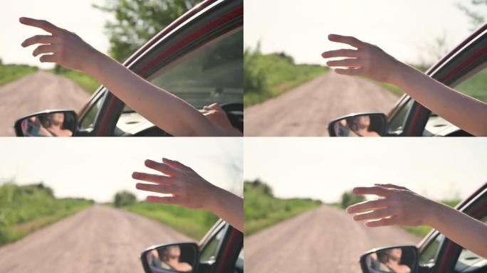 女孩从敞开的车窗上伸出手，捕捉夕阳下的风和阳光。快乐自由女人驾驶红色汽车，旅行，自由，汽车旅游，公路