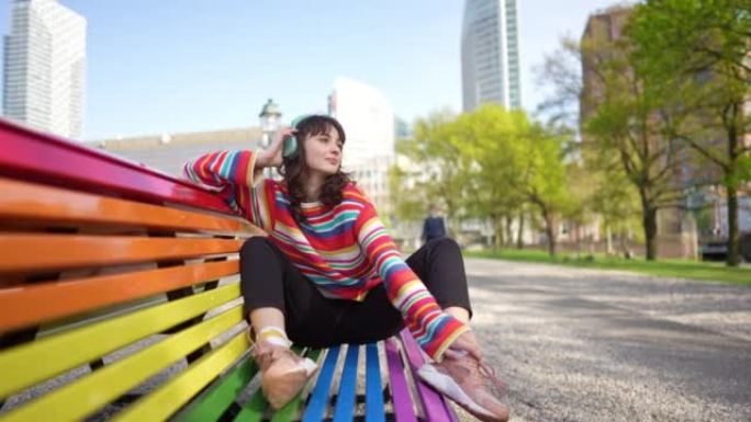 女人在彩虹色的长凳上戴着耳机听音乐