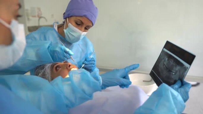 女牙医在咨询过程中看着患者的牙齿和助手所持的x射线