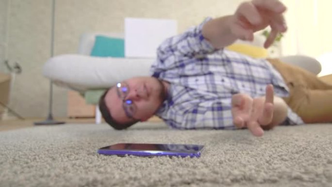 一个穿着衬衫和眼镜的年轻人癫痫发作，他试图到达躺在地板上的智能手机