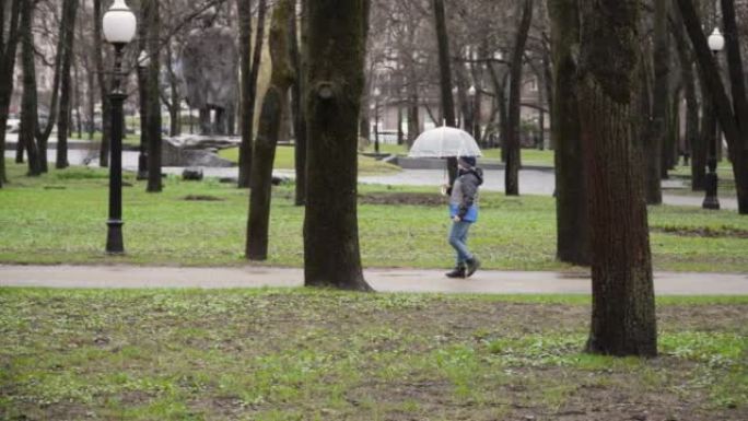 男孩在雨天撑开透明的伞，在公园的路上散步。