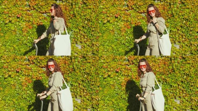 微笑的时尚女性在城市外面的绿色墙壁上