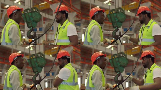 两名身穿制服的非裔美国男性工人戴着安全安全帽，向工业建筑工地的同事解释工业工作。