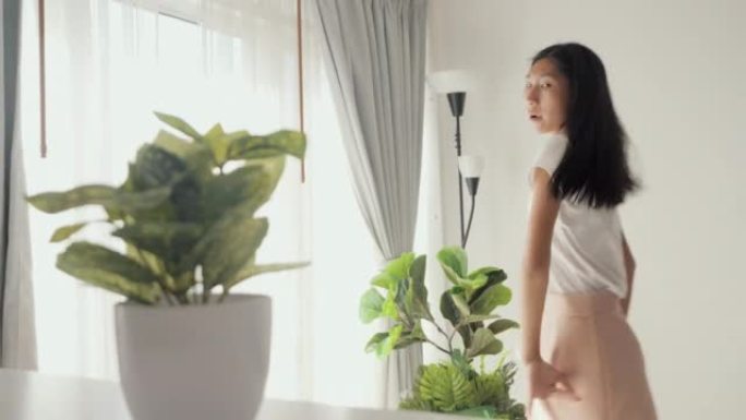 亚洲女孩跳舞，并通过智能手机在家中的窗户附近制作病毒视频，生活方式概念。