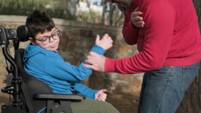 坐在轮椅上四肢瘫痪的小男孩在户外玩耍时享受与父亲的时光。