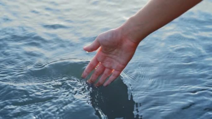 日落时分，雌性手浸入蓝色的水中，在河中流淌着波纹