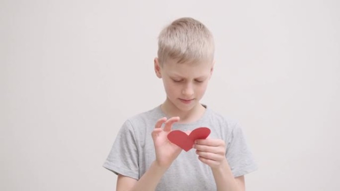 可爱的男孩拿着一张红心形状的情人卡，阅读并微笑着。情人节，2月14日。爱，情感，感觉
