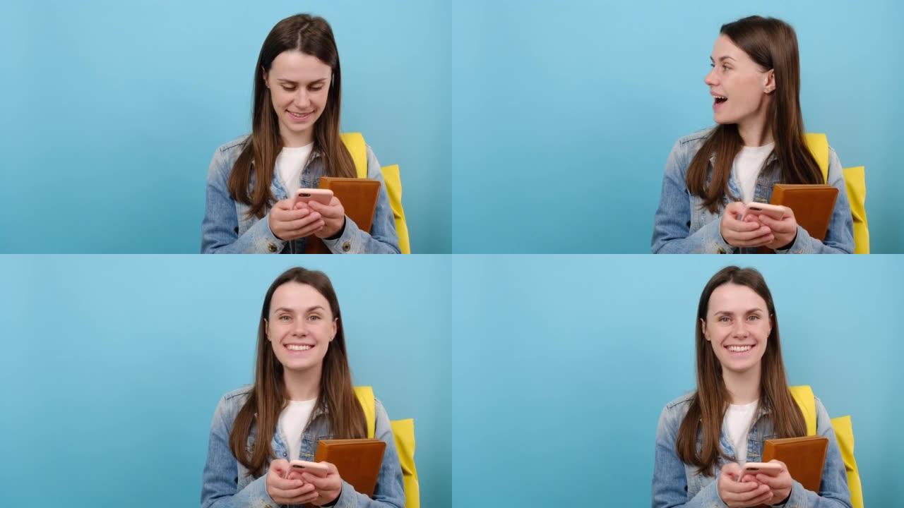 微笑女孩的肖像青少年学生穿牛仔夹克和黄色背包拿着书使用手机在工作区复制空间模拟，孤立在蓝色工作室背景