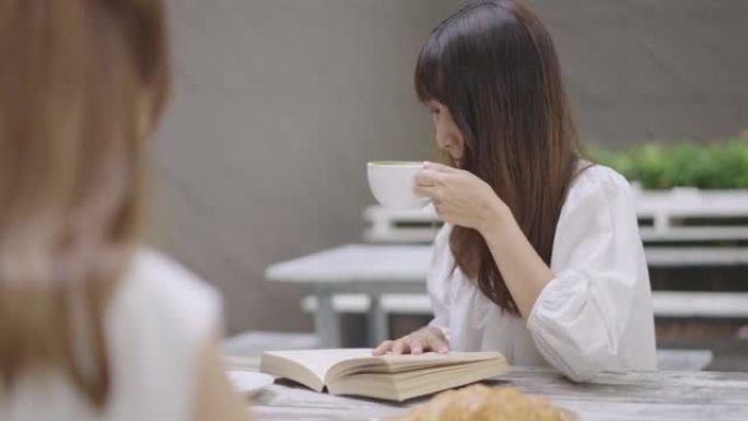 年轻女子和她的朋友坐在咖啡店里，一边读小说，一边喝抹茶。