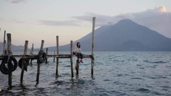 日落时坐在危地马拉阿蒂兰湖码头上的女人