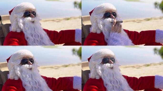 戴着墨镜的圣诞老人躺在热带海滩上的日光浴躺椅上抽古巴雪茄。热带地区的圣诞老人