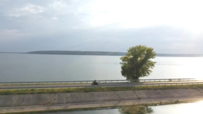 摩托车手在大坝路线上骑摩托车。旅途中开车的人。男子在湖附近的道路上骑着现代运动摩托车，背景是太阳耀斑