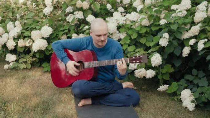 高加索人坐在鲜花丛中的公园里，弹红色原声吉他