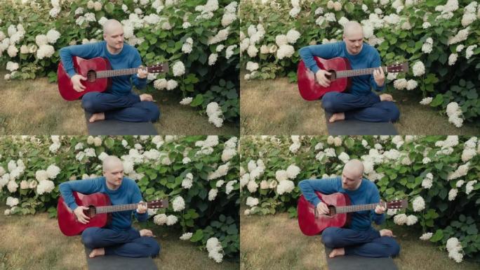 高加索人坐在鲜花丛中的公园里，弹红色原声吉他