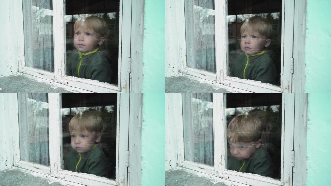 一个孤独的孤儿男孩透过一扇旧窗户看。