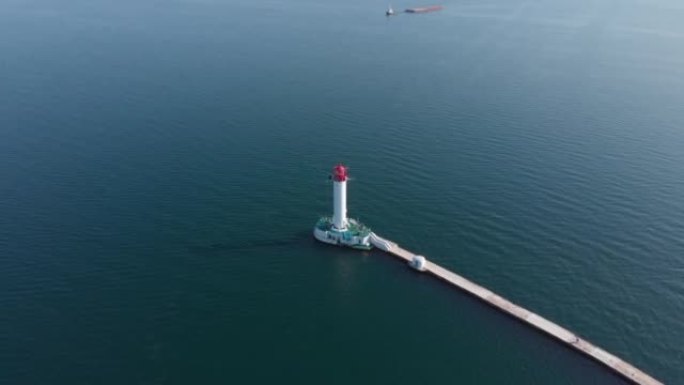 美丽的红白灯塔在海上与蓝色水域无人机轨道高角度拍摄。人们站在海上灯塔。驳船牵引货物