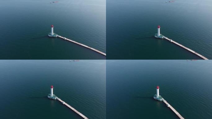 美丽的红白灯塔在海上与蓝色水域无人机轨道高角度拍摄。人们站在海上灯塔。驳船牵引货物