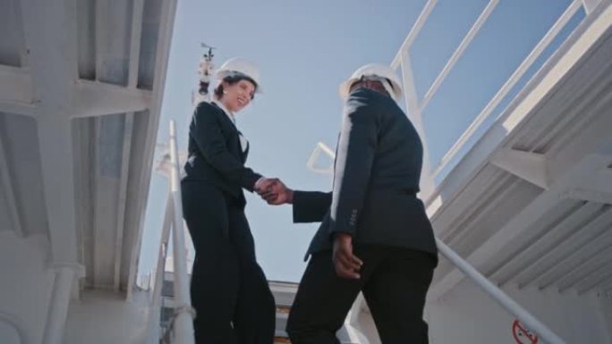 两个工程师在楼梯上握手。两名船舶工程师在走上台阶时握手打招呼。船员在甲板上开会。物流经理达成交易